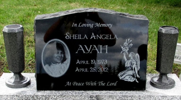 A headstone with a photo, an angel on her knees holding a bouquet of flowers, and two vases on the side built into the monument