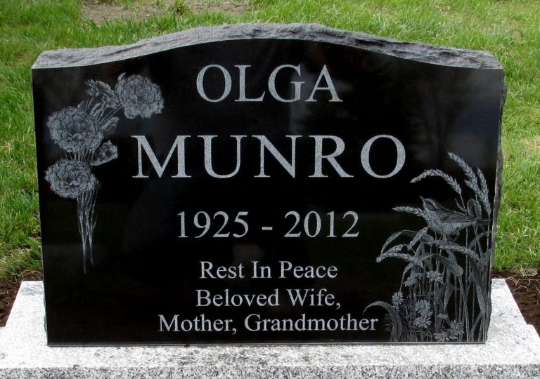 Black granite monument with flowers on the left side and a bird in wheat on the right side. The inscription is in white and reads Olga Munro 1925-2012, Rest in peace beloved wife, mother, grandmother.