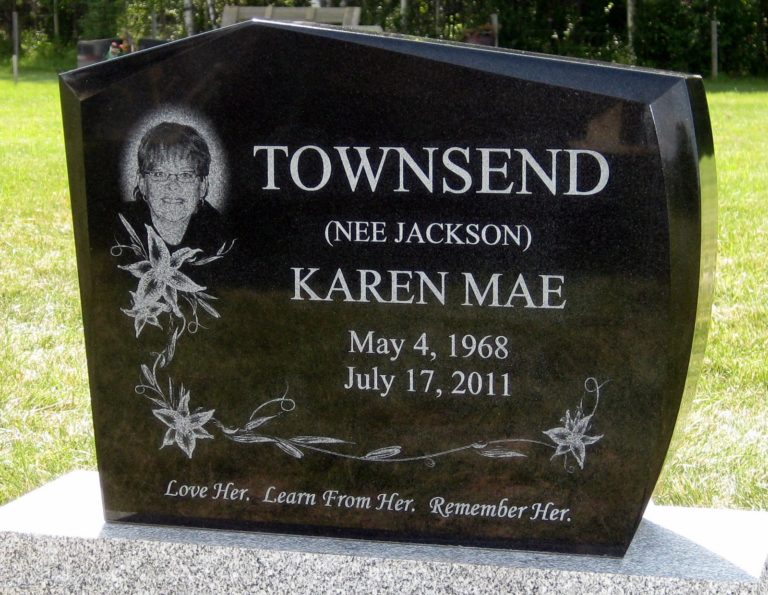 Front of a granite monument that is black. The name reads TOWNSEND (NEE JACKSON) Karen Mar. There is a photo of her as well as flowers surrounding the monument. The bottom is etched with Love Her, Learn from Her. Remember her.