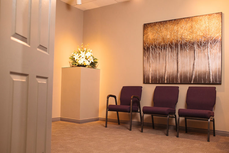 The Viewing room in house at Oliver's Funeral Home. Three chairs, flowers on display, and a photo of trees on the wall