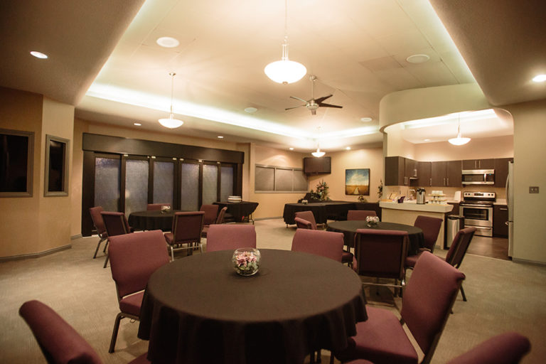 The Tea Room on site at Oliver's Funeral Home. Features round tables with cushioned chairs, a kitchen complete with a microwave, oven, stove, fridge, coffee, and tea.