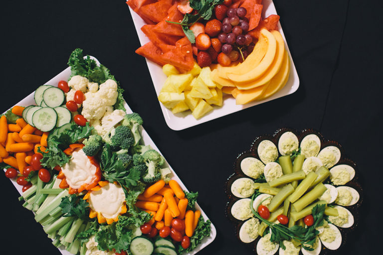 Catering at Oliver's Funeral Home. A vegetable tray with carrots, cucumbers, tomatoes, cauliflower, broccoli, dip, red peppers, orange peppers. A fruit tray with grapes, watermelon, pineapple, and strawberries. A tray of deviled eggs and celery.