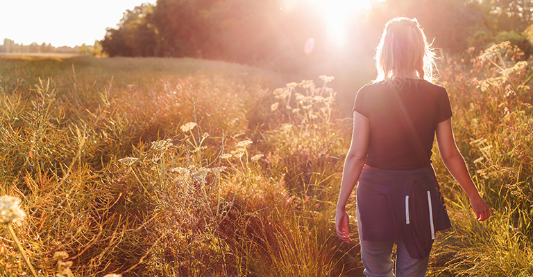 Beautiful young woman walking in field with sunrise