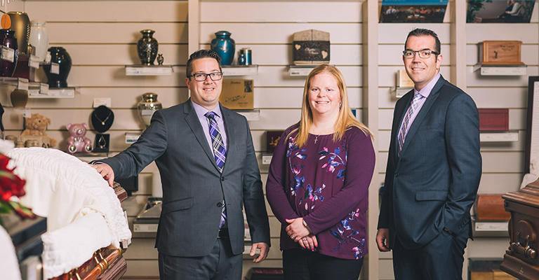 Tracy, Chris, and Craig, the management of Oliver's Funeral Home, stand in front of caskets and urns in Oliver's Funeral Home's on-site show room